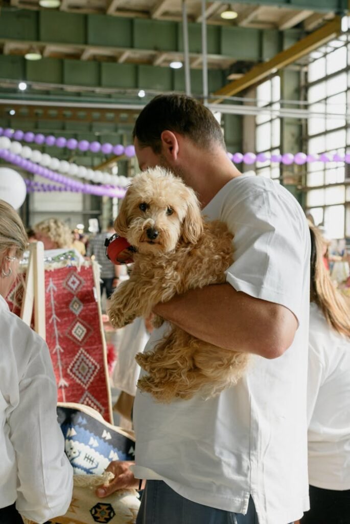 Man holding a fluffy dog indoors at a busy event, featuring colorful decorations.